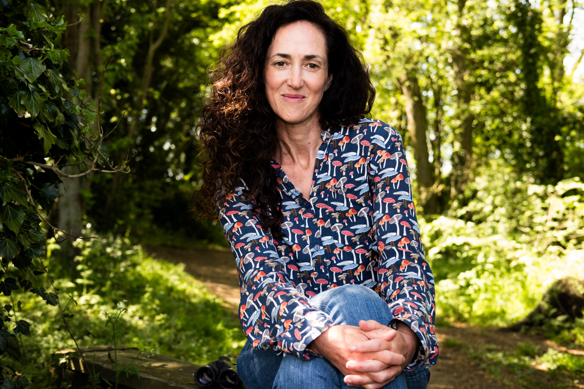Melanie Challenger seated in woodland in 2025.