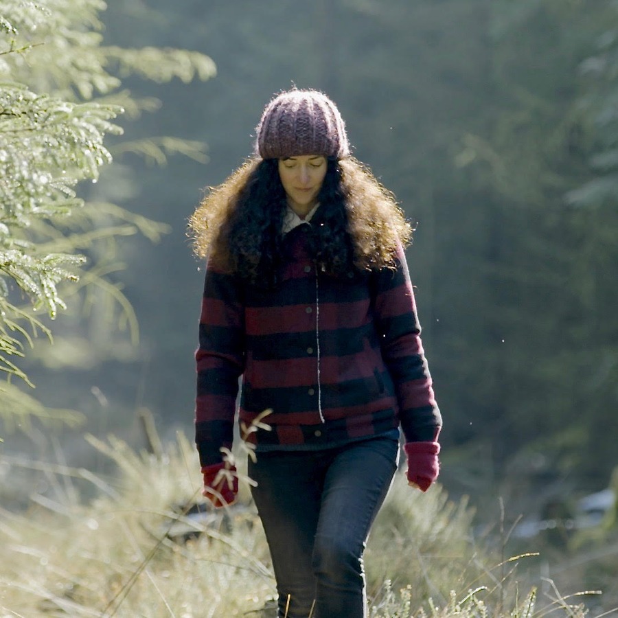 Melanie Challenger walking through a frosted plantation of young conifers.