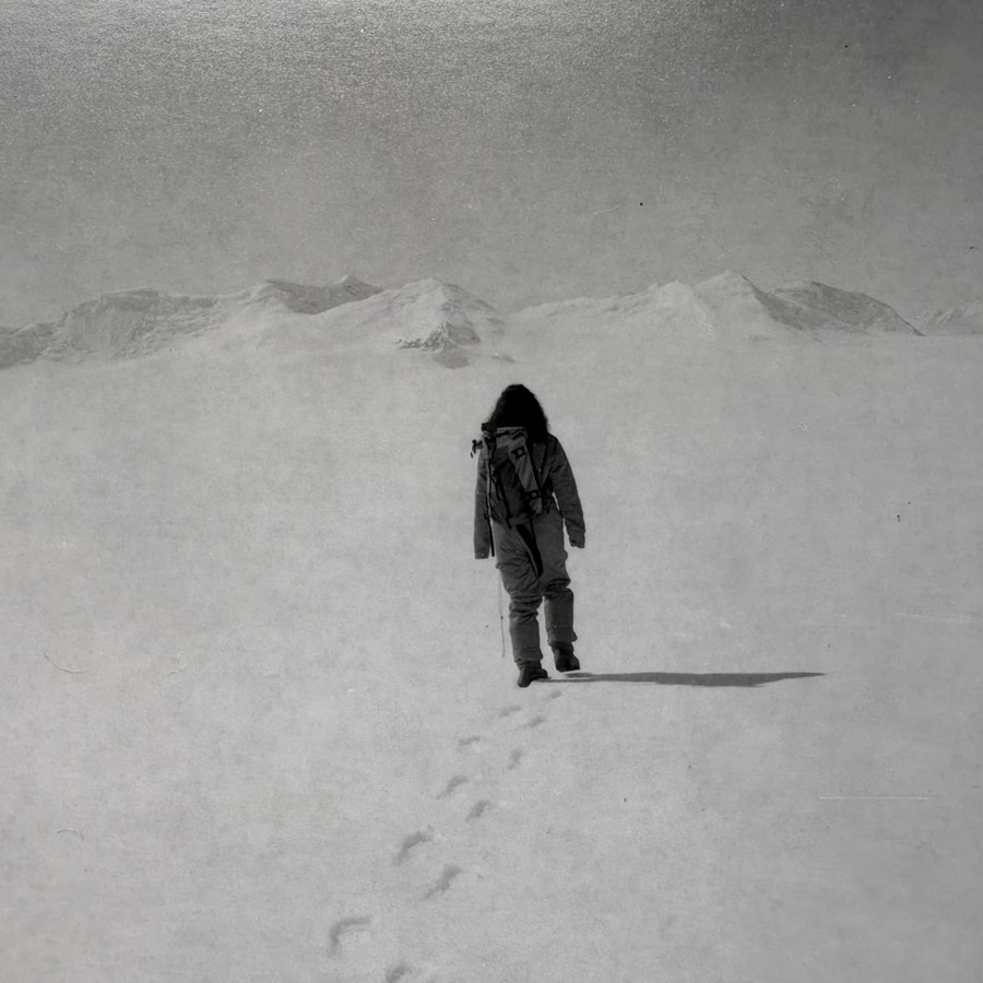 A lone figure walking across snow towards distant mountains.