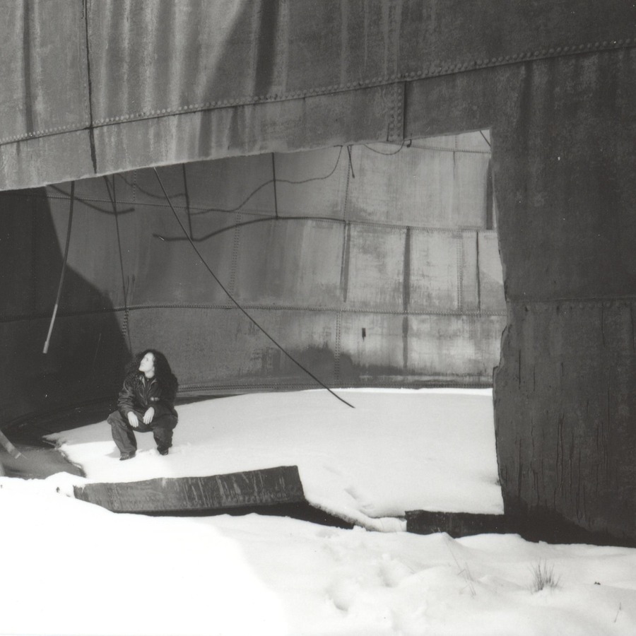 A figure crouching in snow inside a rusted whaling vat
